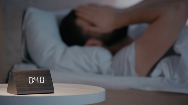 Clock on bedside table near blurred man on bed at night.