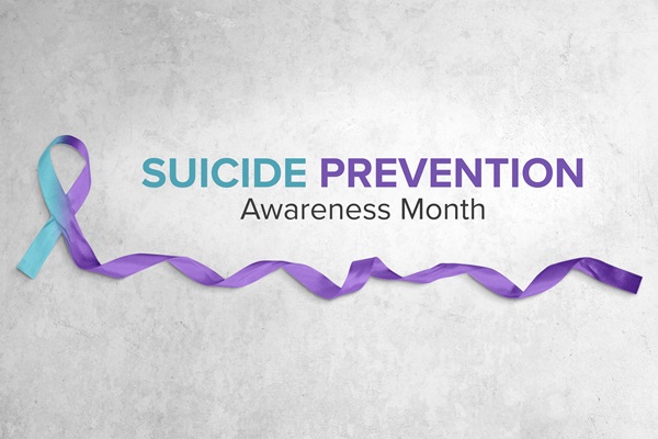 Photo of teal and purple ribbon atop a light gray concrete background with text that reads "Suicide Prevention Awareness Month"