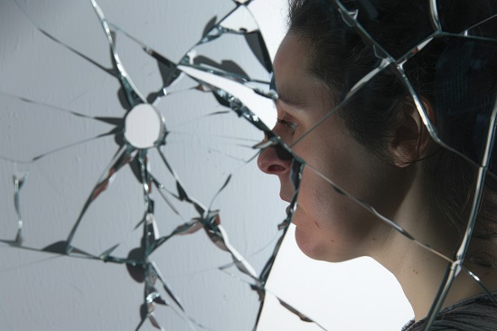 Profile of a man looking through a shattered mirror, with broken glass fragments reflecting different angles of his face, conveying a sense of loss or emotional conflict.