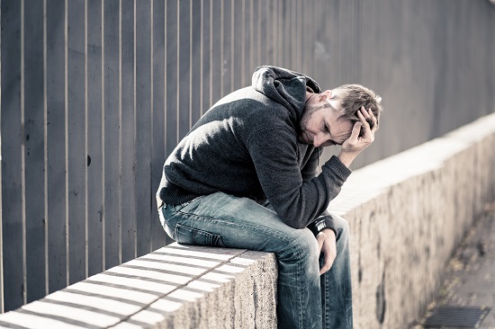 Man sitting on a concrete ledge with his head resting on his hand, appearing stressed, sad, or overwhelmed.